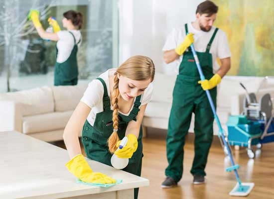 Professional cleaning crew in green overalls sanitizing a modern office using microfiber cloths and mops.