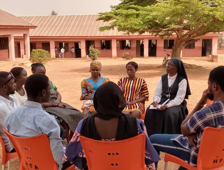A group of diverse community members sitting in a circle for a meeting at an African school courtyard.
