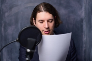Ein Mann hält vor einem Mikrofon ein Blatt Papier in der Hand und liest davon ab