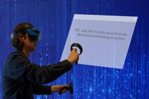 Ein Mann mit VR-Brille und Controller steht vor einer Präsentation auf blauem Hintergrund