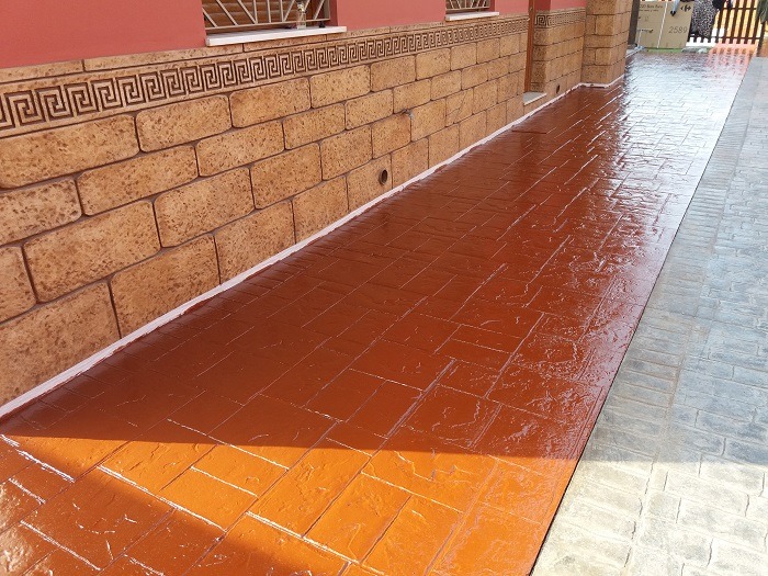 Hormigón impreso en color rojo con acabado brillante, ideal para exteriores elegantes y duraderos.