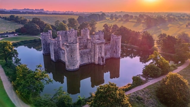 Bodium Castle at sunrise. a moat and trees.