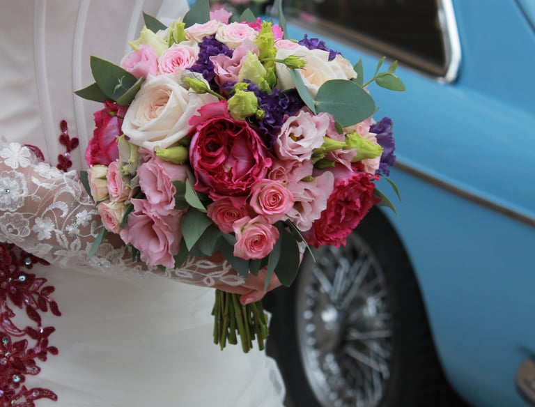 Mariée qui tient un bouquet de fleurs avec en arrière-plan une voiture bleue de collection