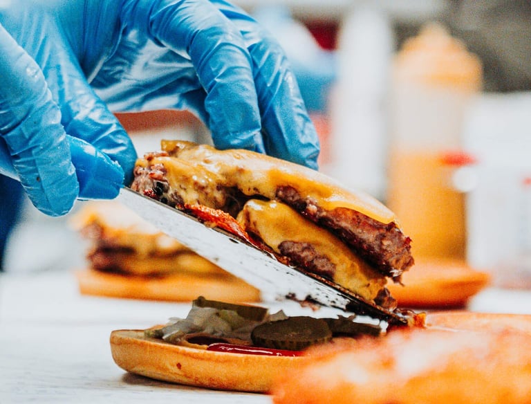 Montaje de hamburguesa doble con cheddar en cocina de Flipa, preparado con guantes y espátula