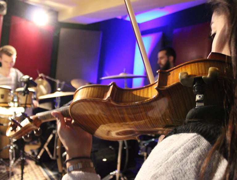 a woman playing a violin in a recording studio with a band