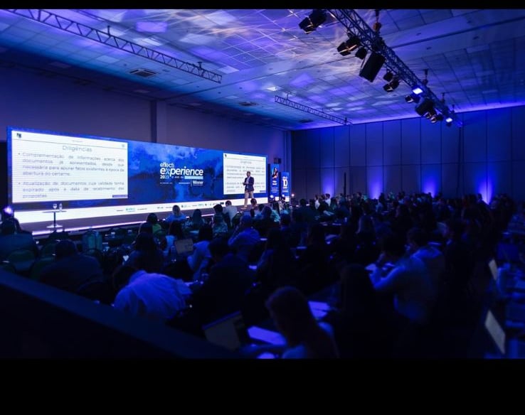 Um palco de evento, com varias pessoas assistindo