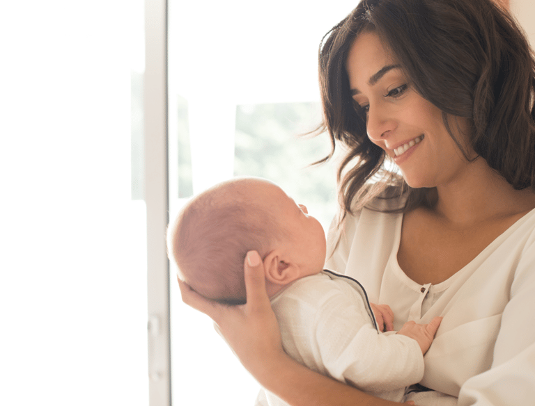 Happy mother holding her little baby in hand and looking at the baby with a smile
