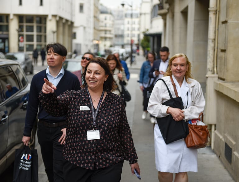 Une guide pointe du doigt un bâtiment en souriant, suivie d'un groupe de visiteurs. Ils marchent dans la rue