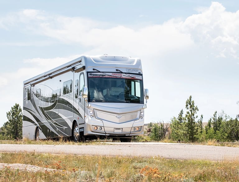 A silver Fleetwood Discovery luxury class A motorhome parked on a scenic road in a rural landscape.