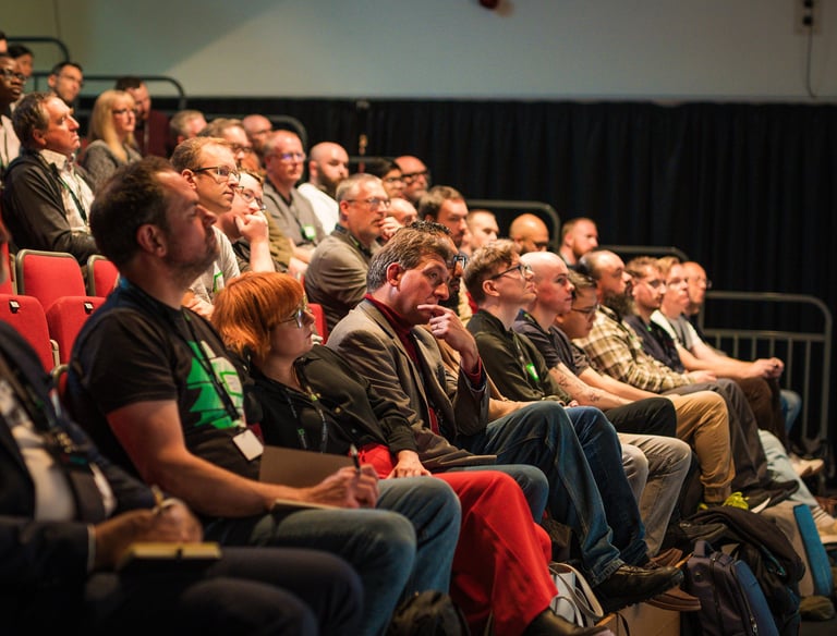 a group of people sitting in a auditorium with people watching a presentation