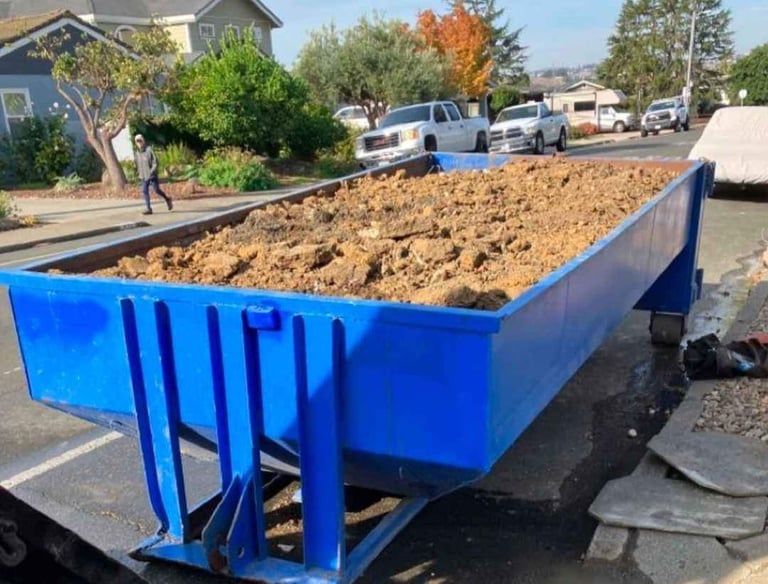 a blue dumpster truck with a large pile of dirt