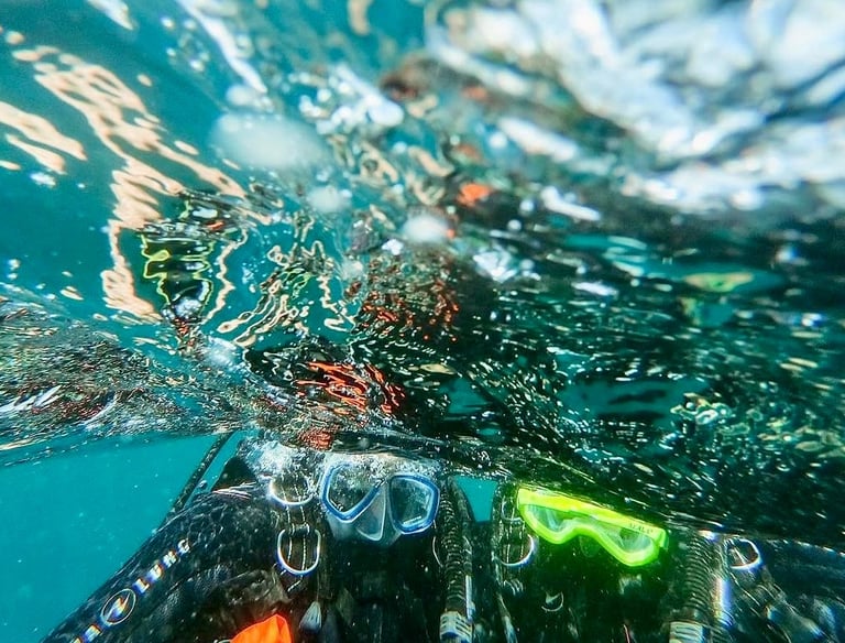 Underwater view of scuba divers wearing masks and gear at the ocean surface with sunlight reflections.