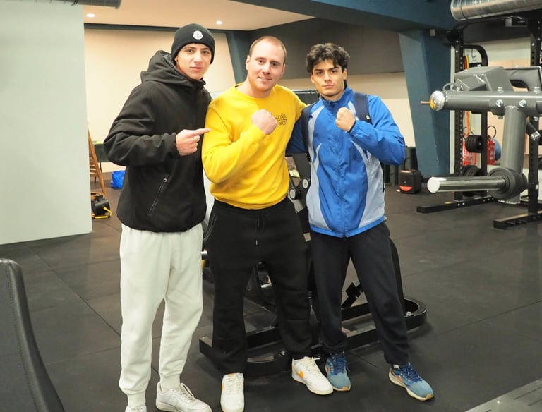 Tre giovani atleti sorridenti posano insieme nella palestra Move 2 Grow a Milano, circondati da attrezzature per l'allenament