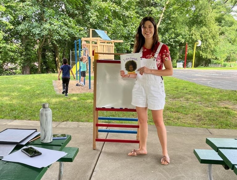 Young woman holding a children's book for a reading in the park event at Crescent Hills park