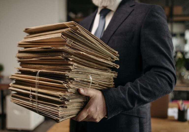 Un hombre de negocios con traje lleva una gran pila de archivos en papel y documentos en una oficina