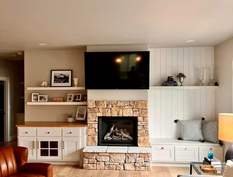 Modern farmhouse living room featuring a stone fireplace, wall-mounted TV, and white built-in shelving.