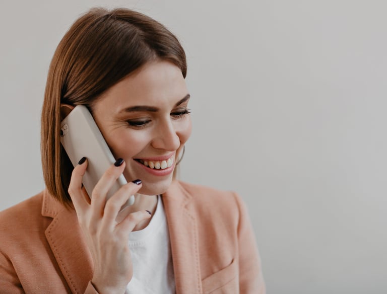Smiling professional woman in a peach blazer talking on a smartphone during a business call.