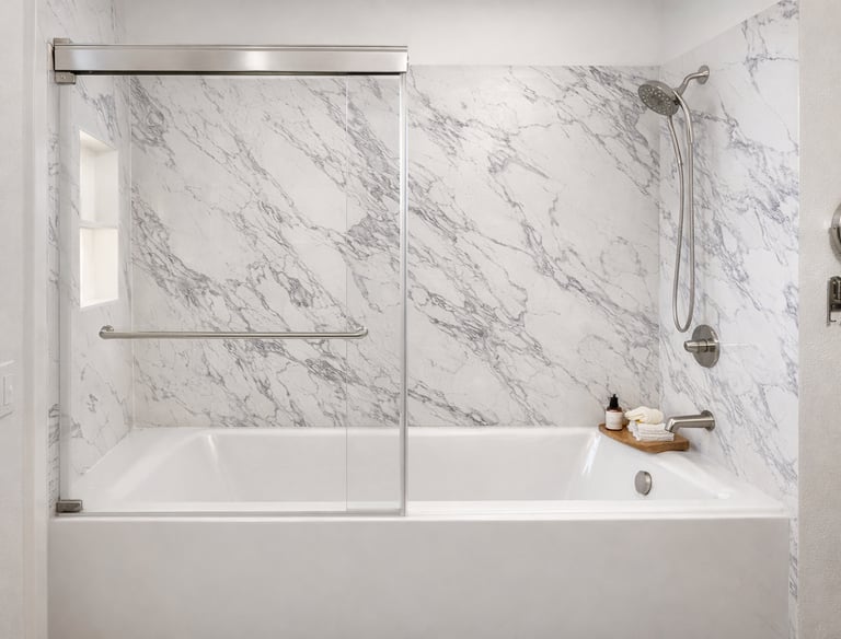 Modern bathroom featuring a white bathtub with marble wall panels and sliding glass doors.