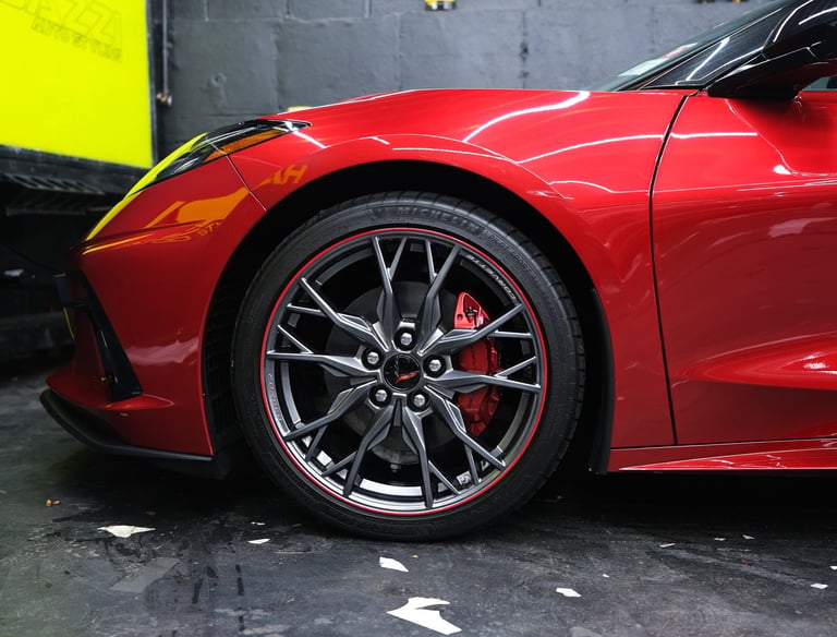 Red Chevrolet Corvette C8 featuring custom alloy wheels and red brake calipers in a professional garage.
