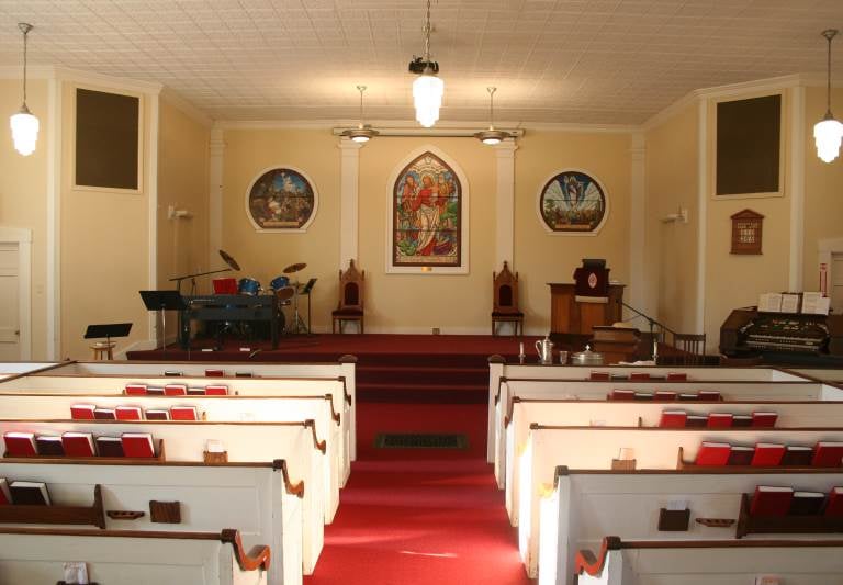 Interior view of a traditional church sanctuary with white pews, red carpet, stained glass windows, and a central altar.