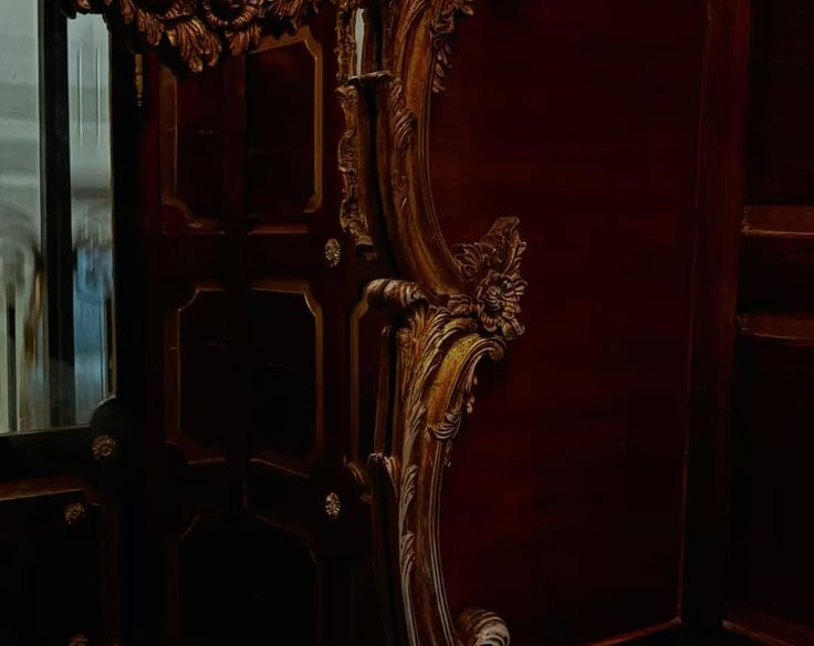 Ornate gilded baroque mirror with cherub carvings and gold acanthus scrollwork against deep crimson