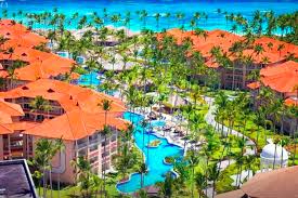 Aerial view of a tropical beachfront resort featuring orange-roofed villas, palm trees, and winding blue swimming pools.