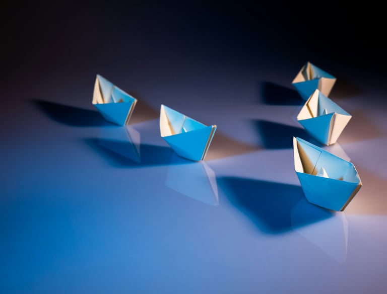 A strategic formation of paper boats arranged on a blue surface, led by one of them