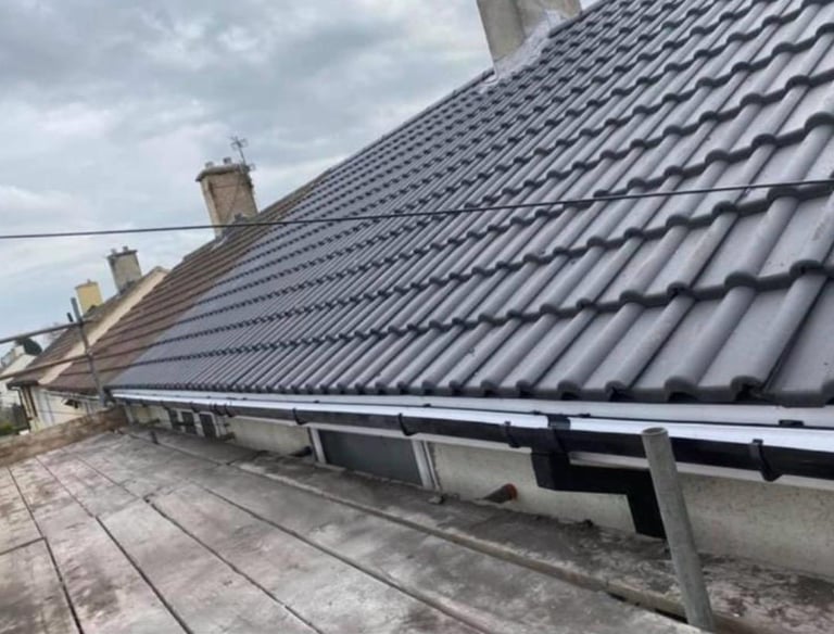 Newly installed black plastic guttering on a tiled residential roof with professional scaffolding.