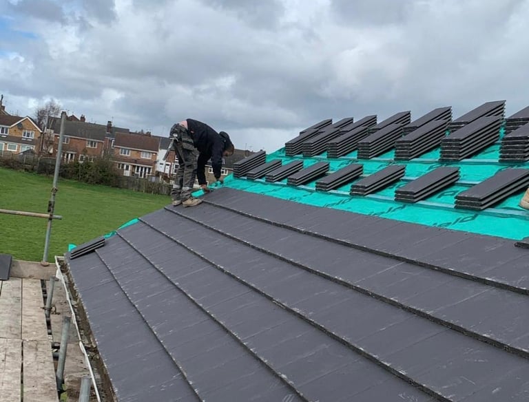 A roofer installs dark grey concrete roof tiles on a house with a green breathable membrane.