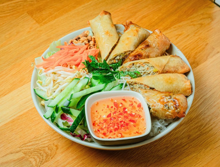 a bowl of vermicelli salad with spring rolls.