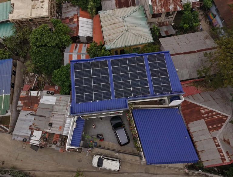 An aerial drone shot of a residential house with a bright blue metal roof featuring a large array of black solar panels