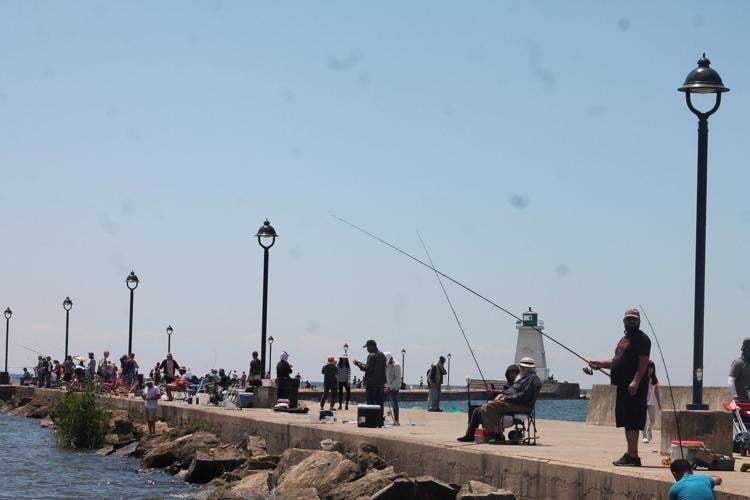 Anglers fishing on a concrete pier with a white lighthouse and lampposts under a clear blue sky.