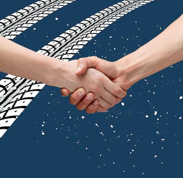 Dos manos de diferentes tonos de piel dándose un apretón de manos en el centro de un fondo azul con dos huellas de neumáticos
