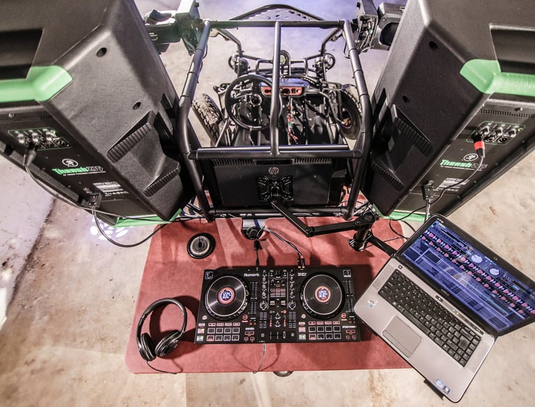 Professional DJ setup on wheels with a controller, laptop, headphones, and large speakers.