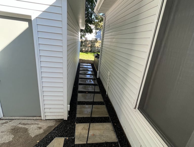 Narrow side yard path with modern concrete pavers and black lava rock mulch between white houses.