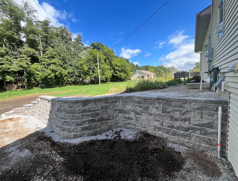 New gray stone retaining wall installed in a backyard landscape next to a residential house.