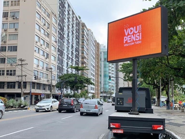 Digital LED billboard truck advertising on a busy city street near high-rise buildings and trees.