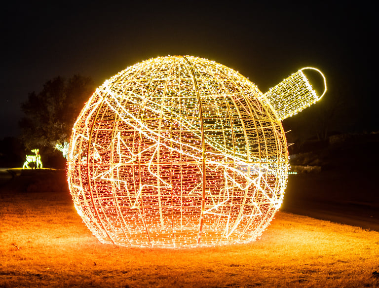 Large outdoor commercial Christmas ornament light display lit with warm gold and red LEDs at night.