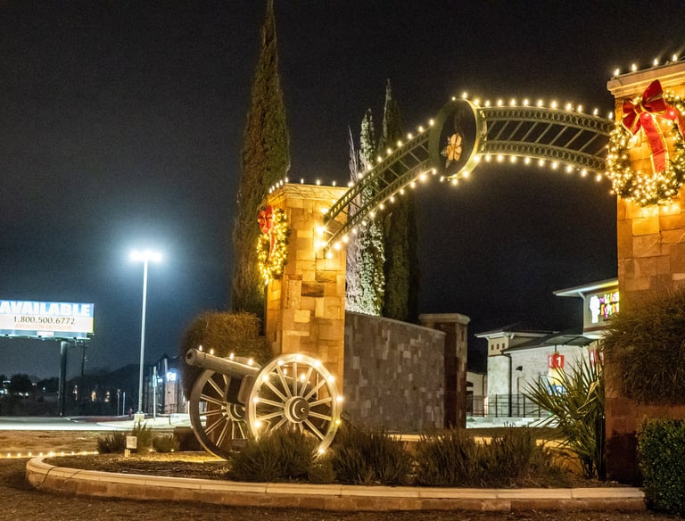 Stone archway with Christmas lights and a decorative cannon at a commercial shopping center at night.