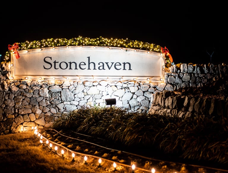 HOA community entrance sign, adorned with festive Christmas lights, at night.