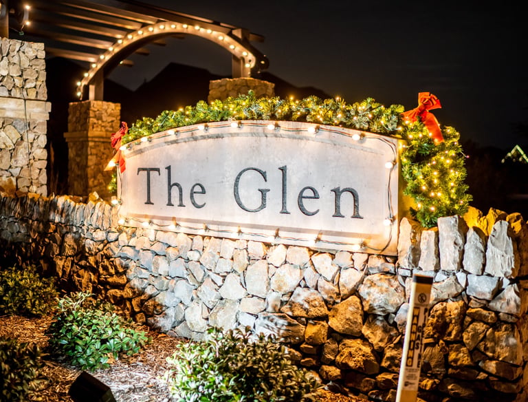 neighborhood stone entrance sign decorated with Christmas lights and festive holiday greenery at night.