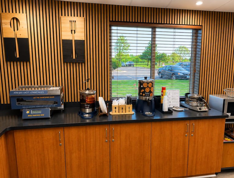 Hotel breakfast bar with an automatic pancake machine, syrup, butter, and waffle makers.
