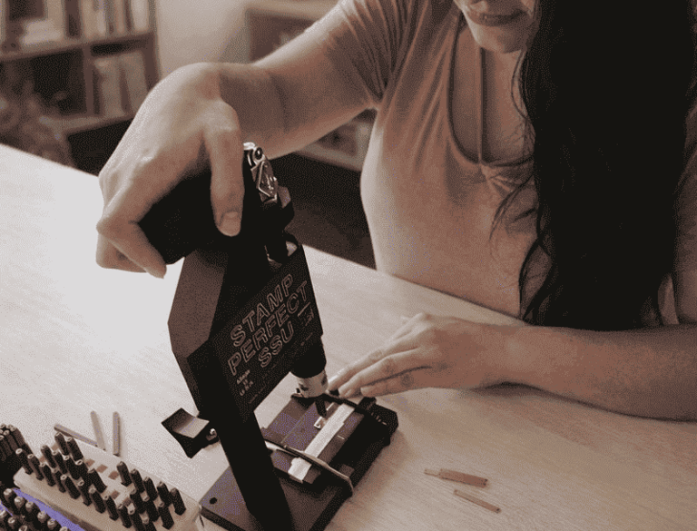 Una mujer utiliza una herramienta de estampado de metal para grabar joyas personalizada