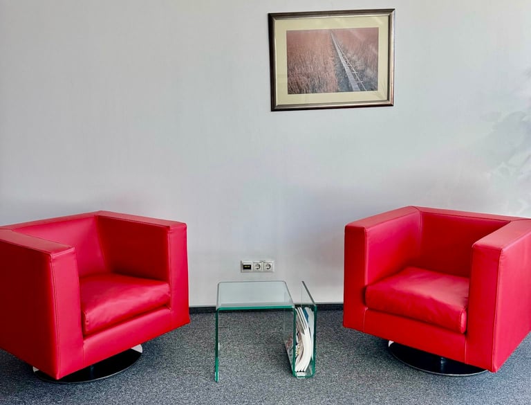 Two modern red leather swivel armchairs in a minimalist office waiting area with a glass side table.