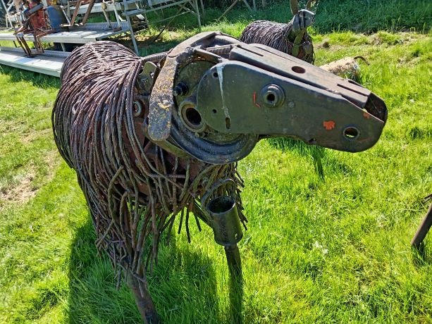 Rustic metal sheep sculpture crafted from recycled farm tools and wire standing in a green field.