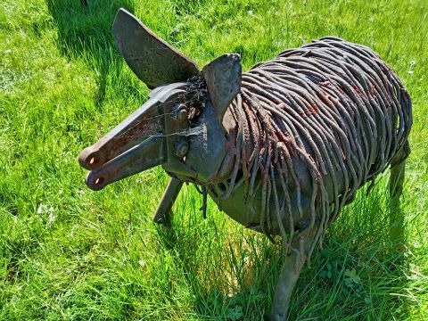 Rustic scrap metal pig sculpture handcrafted from recycled iron parts in a green grassy field.