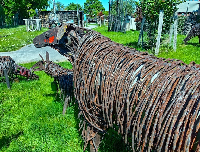 Rustic metal sheep sculpture made of recycled rebar and scrap metal in a sunny garden.