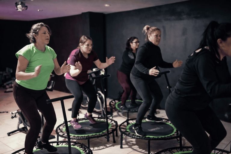 Un grupo de mujeres participando en una clase de salto en trampolín de alta energía en un gimnasio.