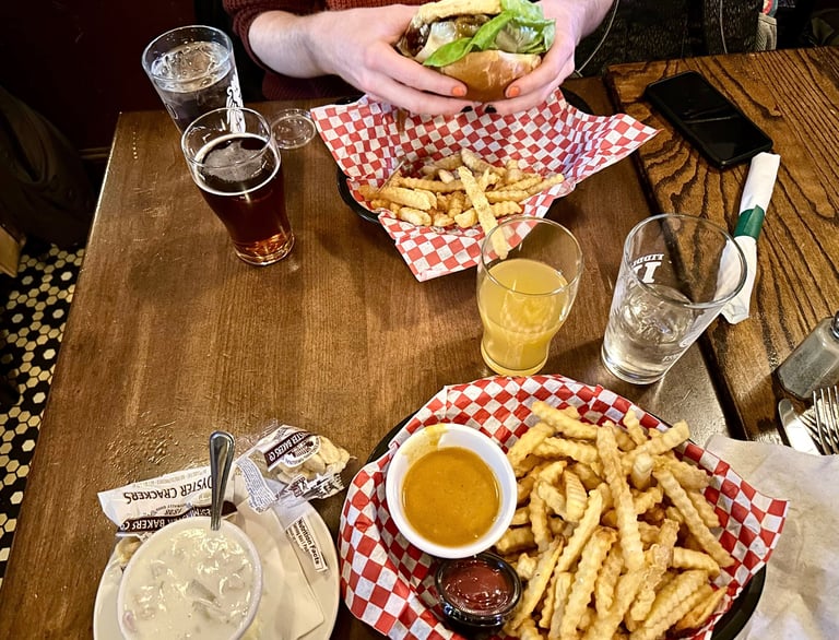 a person holding a cheeseburger with clam chowder and curry fries on the table