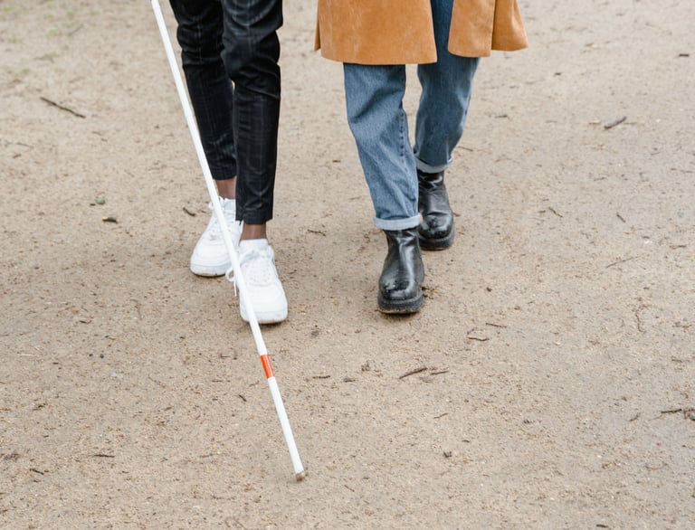 Un homme mal voyant avec sa canne accompagné d' une aidante marchant sur un chemin